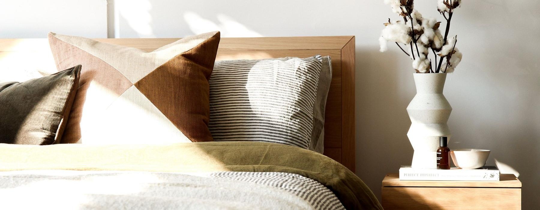 swath of sunlight shines across a well made bed and bedside table with a vase of cotton plants