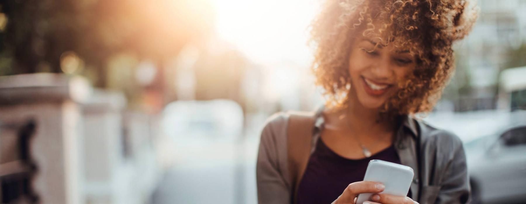 woman texts on her phone as she walks through the city